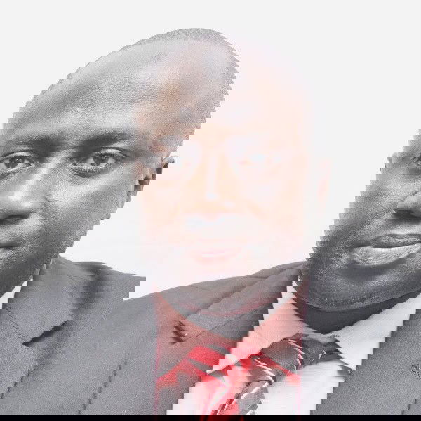 Malick Mboob A man wearing a black suit jacket, light pink dress shirt, and red striped tie poses for a formal portrait against a plain white background.